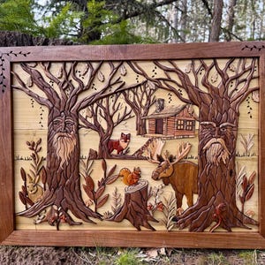 May include: A wooden relief carving depicting a forest scene with trees, a cabin, and wildlife. The artwork features a moose, fox, and squirrel, all carved in various shades of brown and tan. The frame is a dark brown, and the background is a light tan.