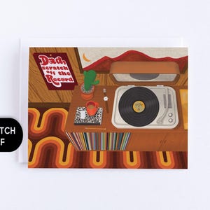 Könnte beinhalten: Eine Grußkarte mit einer Illustration eines Plattenspielers auf einer Holzkonsole, einem Kaktus, einer Uhr, einer roten Tasse und einem Notizbuch. Der Text lautet Dad, scratch off the Record. Der Hintergrund zeigt ein wellenförmiges Teppichmuster.
