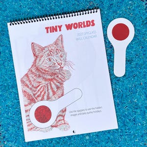 Peut inclure: Un calendrier mural 2027 Tiny Worlds à reliure spirale, présentant une illustration au trait rouge d'un chat faisant sa toilette. Le calendrier comprend un outil loupe manuel blanc avec une lentille circulaire rouge pour voir les images cachées.