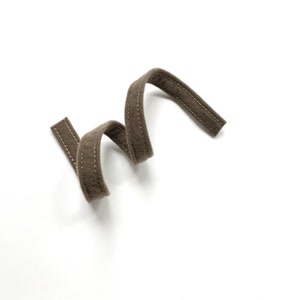 May include: A brown fabric cord with a stitched seam, coiled into a spiral shape.
