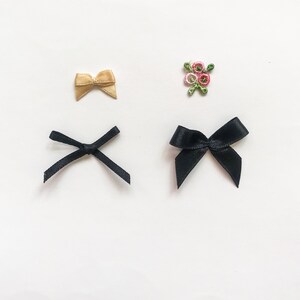 May include: Three different ribbon bows, two black and one beige, and a small embroidered flower design.