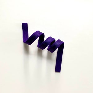 May include: A purple ribbon is curled into a spiral shape on a white background.