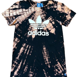 May include: Black tie-dye t-shirt with a white Adidas logo and the word "adidas" printed on the front.