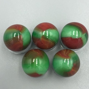 May include: Five glass marbles with a swirling red and green pattern. The marbles are arranged in a semi-circle on a gray surface.