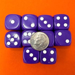 May include: A collection of nine purple six-sided dice with white pips, arranged in a grid pattern. A silver United States dime coin is placed on top of the center dice to provide a scale reference for the size of the individual game pieces.