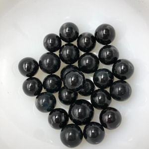 May include: A collection of black glass marbles in a white bowl. The marbles are smooth and shiny.
