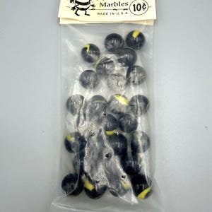May include: A clear plastic bag filled with black and yellow marbles. The bag has a paper header with the text "Bumblebees Marbles" and a cartoon bee illustration. The text "Made in U.S.A." is also visible.