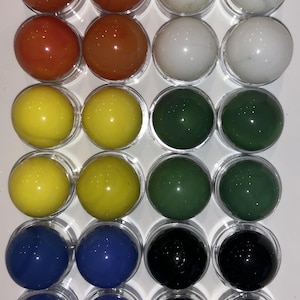May include: A set of 20 glass marbles in various colors, including red, yellow, green, blue, and black. The marbles are arranged in rows of four, with each marble sitting in a clear plastic container.