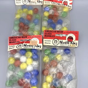 Puede incluir: Cuatro bolsas de plástico selladas de canicas de vidrio Marble King, cada una etiquetada como American Made Glass Marbles con un conteo de 25 e incluye un shooter. Las bolsas contienen esferas de vidrio translúcidas y opacas multicolores.