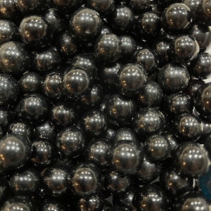 May include: A large pile of black obsidian spheres. The spheres are smooth and shiny, and they reflect light.