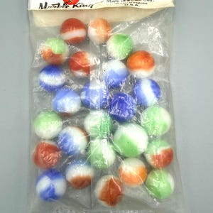 Puede incluir: Una bolsa de plástico transparente que contiene canicas de vidrio variadas en tonos naranja, verde y azul con remolinos blancos. La tarjeta superior dice "our marbles crown kings" y "Marble King" con "Made in Paden City, West Virginia, U.S.A."