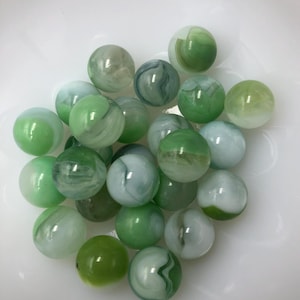 May include: A collection of green and white marbles with swirling patterns. The marbles are arranged in a pile on a white surface.