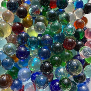 May include: A collection of colorful glass marbles in various sizes and shades. The marbles are a mix of transparent, opaque, and iridescent, with colors including red, blue, green, yellow, and black. The marbles are scattered, creating a playful and visually appealing arrangement.
