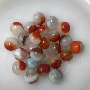 May include: A collection of 20 red, white, and orange swirl glass marbles. The marbles are arranged in a pile on a white surface.