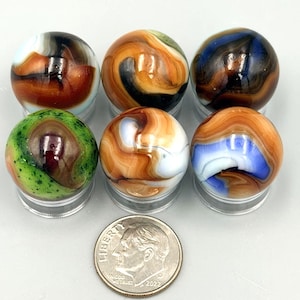 May include: Six spherical glass marbles with swirling patterns in colors including green, orange, brown, white, and blue, arranged in two rows of three. A silver-colored United States dime is placed in front for scale, showing the size.
