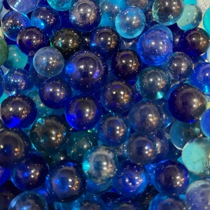 Puede incluir: Una imagen de primer plano de un gran grupo de canicas de vidrio azules y verde azulado. Las canicas están dispuestas en un patrón aleatorio, creando una superficie visualmente atractiva y texturizada.