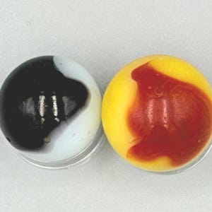 May include: Two spherical glass marbles. One marble features a white base with a large, opaque black swirl pattern. The second marble has a bright yellow base with a prominent, translucent reddish-orange swirl pattern across its surface.