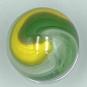 May include: A spherical glass marble featuring a clear base with a swirling internal pattern of opaque yellow and translucent green glass. The surface is smooth and reflective, showing a distinct curved design within the transparent sphere.