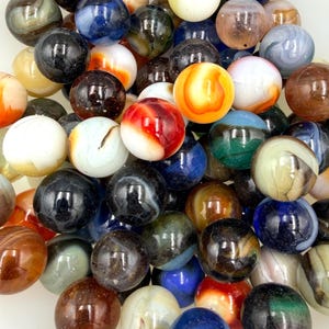 May include: A collection of numerous glass marbles in various colors and patterns, including solid, swirled, and translucent designs. The spheres feature shades of blue, red, orange, black, white, brown, and green, creating a dense, multi-colored cluster.