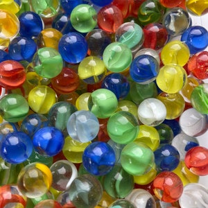 Könnte beinhalten: Eine große Sammlung bunter Glasmurmeln in verschiedenen Blautönen, Grüntönen, Rottönen, Gelbtönen und Weißtönen. Die Murmeln sind in einem zufälligen Muster angeordnet und bilden ein optisch ansprechendes und lebendiges Display.