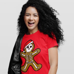 Pode incluir: Uma mulher vestindo uma camiseta vermelha com um esqueleto de gengibre usando um chap&eacute;u de Papai Noel. Ela est&aacute; sorrindo e tem cabelo preto encaracolado. Ela est&aacute; vestindo uma jaqueta de couro preta.
