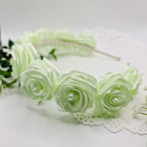 May include: A light green headband with five fabric rose embellishments. The headband is made of a thin, flexible material and is perfect for adding a touch of elegance to any outfit.