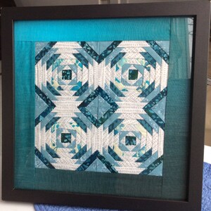 May include: A framed quilt with a geometric pattern in shades of blue and white. The quilt is surrounded by a teal border.