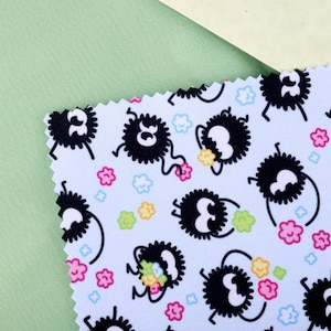May include: A light blue fabric sample with a repeating pattern of black, fluffy creatures with white eyes and legs, holding colorful flowers. The design includes pink, yellow, and blue floral accents. The fabric is set against a light green and cream background.