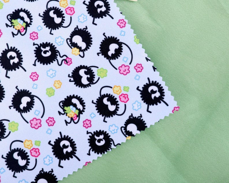 May include: A light blue fabric with a repeating pattern of black, fluffy creatures with white eyes and legs, holding colorful flowers. Pink, yellow, and green flowers and small blue clouds are scattered across the fabric. A light green fabric is in the background.