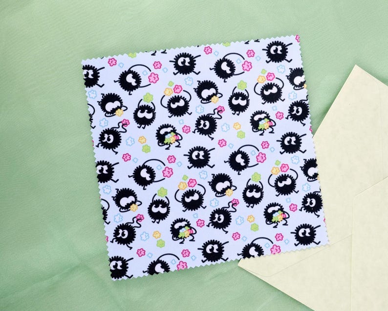 May include: A square card with a white background featuring a repeating pattern of black, fluffy creatures with large eyes, surrounded by colorful star and flower shapes. The card has a scalloped edge and is next to a cream-colored envelope.