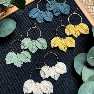 May include: Four pairs of hoop earrings with three macrame leaf charms hanging from each hoop. The earrings are in four different colours: teal, yellow, green, and white.