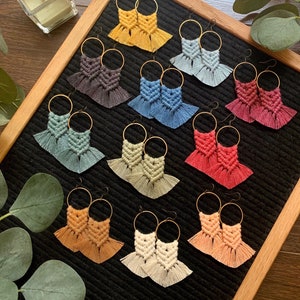 May include: A set of 10 pairs of handmade macrame earrings in various colors, including yellow, blue, green, red, and orange. Each pair features a geometric design with fringe details.
