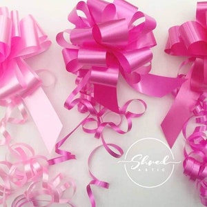 May include: Three pink satin ribbon bows with curled ribbon tails. The bows are arranged in a row on a white surface. The text "Shred Attic" is visible in the lower right corner of the image.