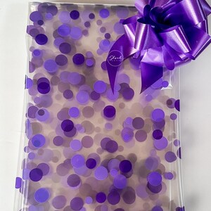 May include: A clear gift bag with a purple polka dot pattern and a large purple satin bow. The bag has the text "Shreel Gifts" printed on it.