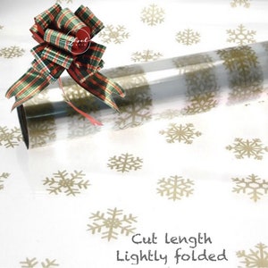 May include: Clear wrapping paper roll with gold snowflake design. A red, green, and gold plaid bow is attached. The text "Cut length, lightly folded" is visible. Ideal for Christmas.