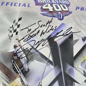 May include: A commemorative Brickyard 400 program cover featuring a graphic of a person waving a checkered flag. The cover includes the text "OFFICIAL" and "BRICKYARD 400" with a handwritten black ink autograph that reads "To Scott Best Wishes".