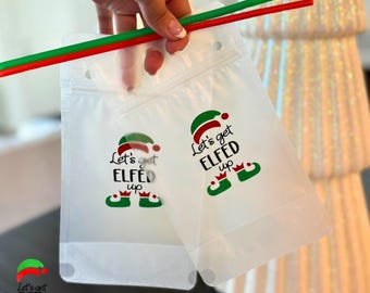 May include: Two clear plastic pouches with the text "Let's get ELFED up" and an elf hat and shoe design. The pouches have a zipper closure and a hole for a straw. A red and green straw is held above the pouches.