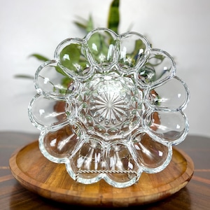 Pode incluir: Prato de servir de vidro transparente com design floral. O prato tem uma área central padronizada e compartimentos em forma de pétala na borda. Ele está em uma bandeja de madeira com um suporte de metal, mostrando um estilo vintage.