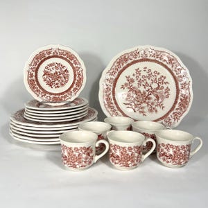 Puede incluir: Un juego completo de vajilla vintage en blanco con un estampado floral rojo. El juego incluye platos, cuencos y tazas. Los platos tienen un borde festoneado. Las tazas tienen un asa.
