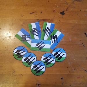 May include: A set of six round stickers and five rectangular stickers featuring a blue, green, and black design with a stylized image of three trees and arrows.