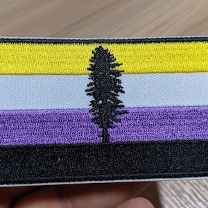 May include: A yellow, white, purple, and black embroidered patch with a stylized tree in the center. The patch is a representation of the non-binary pride flag.