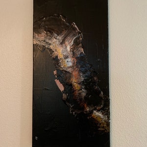 May include: Abstract painting on canvas with a black background and a large, textured, brown, white, and gold shape in the center.