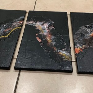 May include: Three black canvas paintings with abstract designs in gold, white, and orange. The designs are reminiscent of flowing water or a river.