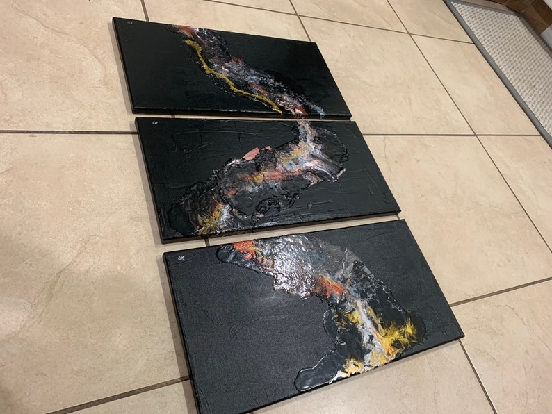 May include: Three black canvas panels with abstract art featuring gold, white, and pink paint. The panels are arranged horizontally and are ready to be hung on a wall.