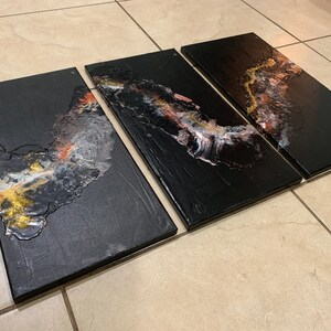 May include: Three black canvas panels with abstract art featuring gold, white, and pink paint. The panels are arranged horizontally and are ready to be hung on a wall.