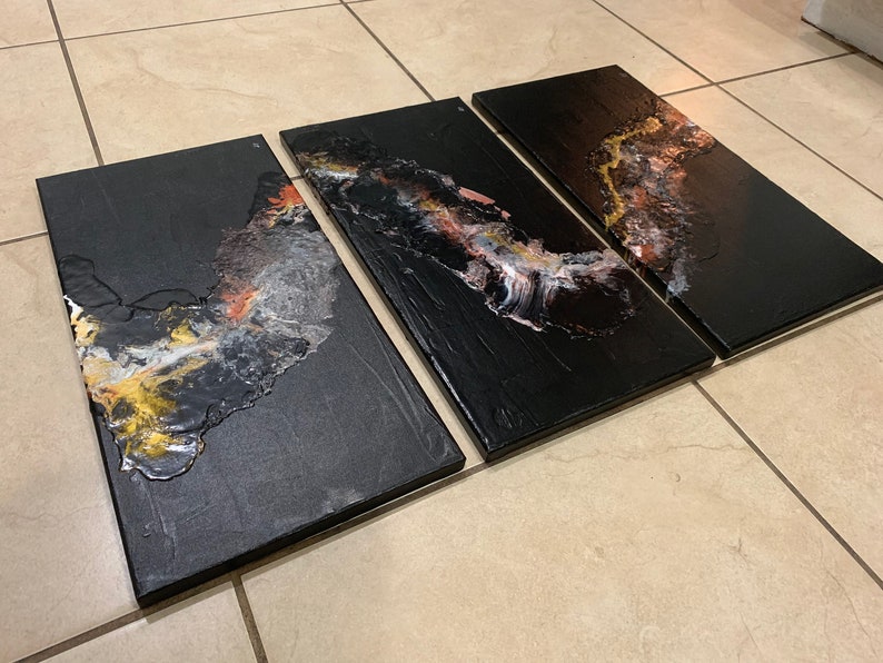 May include: Three black canvas panels with abstract art featuring gold, white, and pink paint. The panels are arranged horizontally and are ready to be hung on a wall.