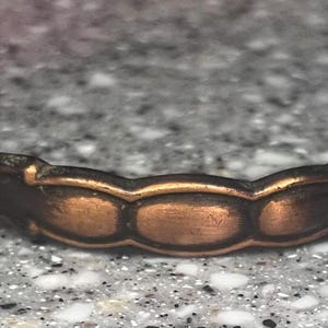 May include: A bronze-coloured drawer pull with a decorative design. The pull has a curved shape with a series of oval-shaped details in the centre and silver-coloured knobs on each end. The hardware is designed for furniture.