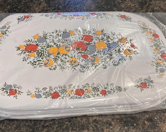 May include: A set of white oval serving trays with a floral design featuring red, yellow, and blue fruits and flowers. The trays are wrapped in clear plastic. The floral design is repeated around the edges of the trays.