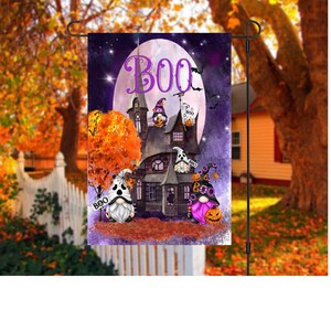 Può includere: Una bandiera da giardino di Halloween viola e arancione con una casa infestata, una luna piena e tre gnomi. Gli gnomi indossano cappelli e tengono zucche. La bandiera dice "BOO" in grandi lettere viola.