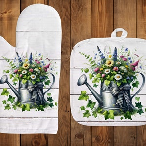 Könnte beinhalten: Ein Set aus zwei weißen Baumwoll-Topflappen mit einem Blumendesign. Das Design zeigt eine antike Gießkanne, gefüllt mit einem Strauß bunter Blumen und grünem Efeu.